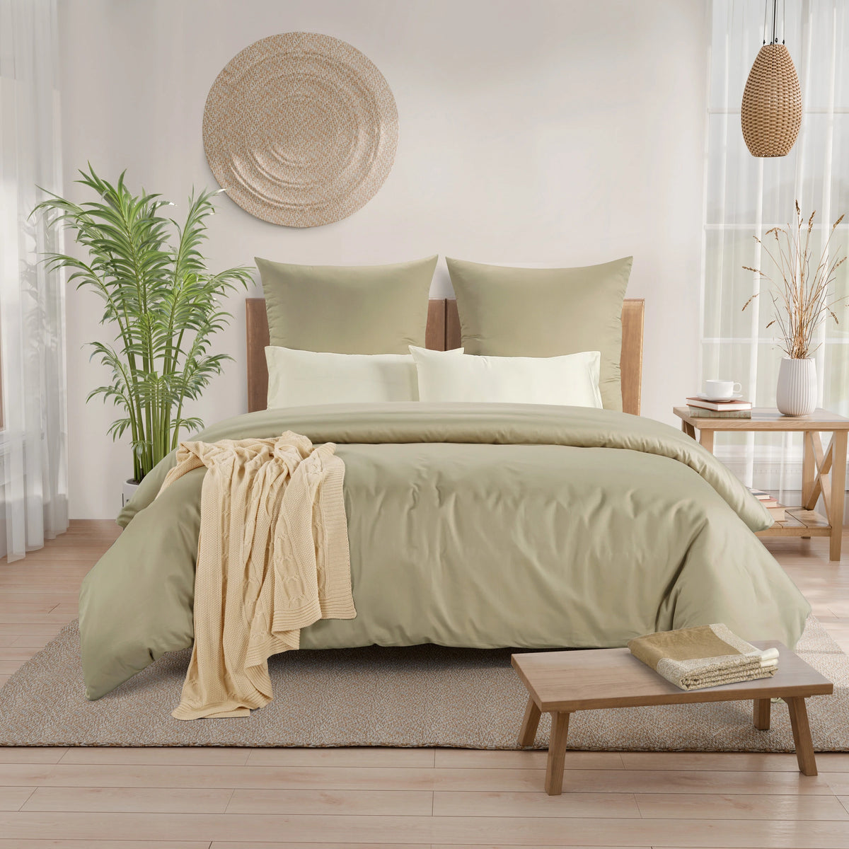 A neatly made bed in a bright, modern bedroom featuring a sage oak color duvet cover and matching pillow shams, accented with white pillows and a draped cream throw blanket.