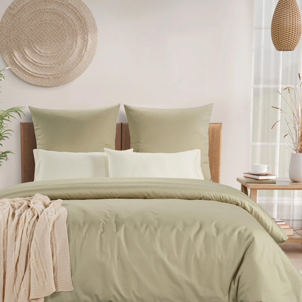 A neatly made bed with sage green bedding, including a duvet cover, two matching pillow shams, and two white accent pillows, styled in a bright, modern bedroom setting.