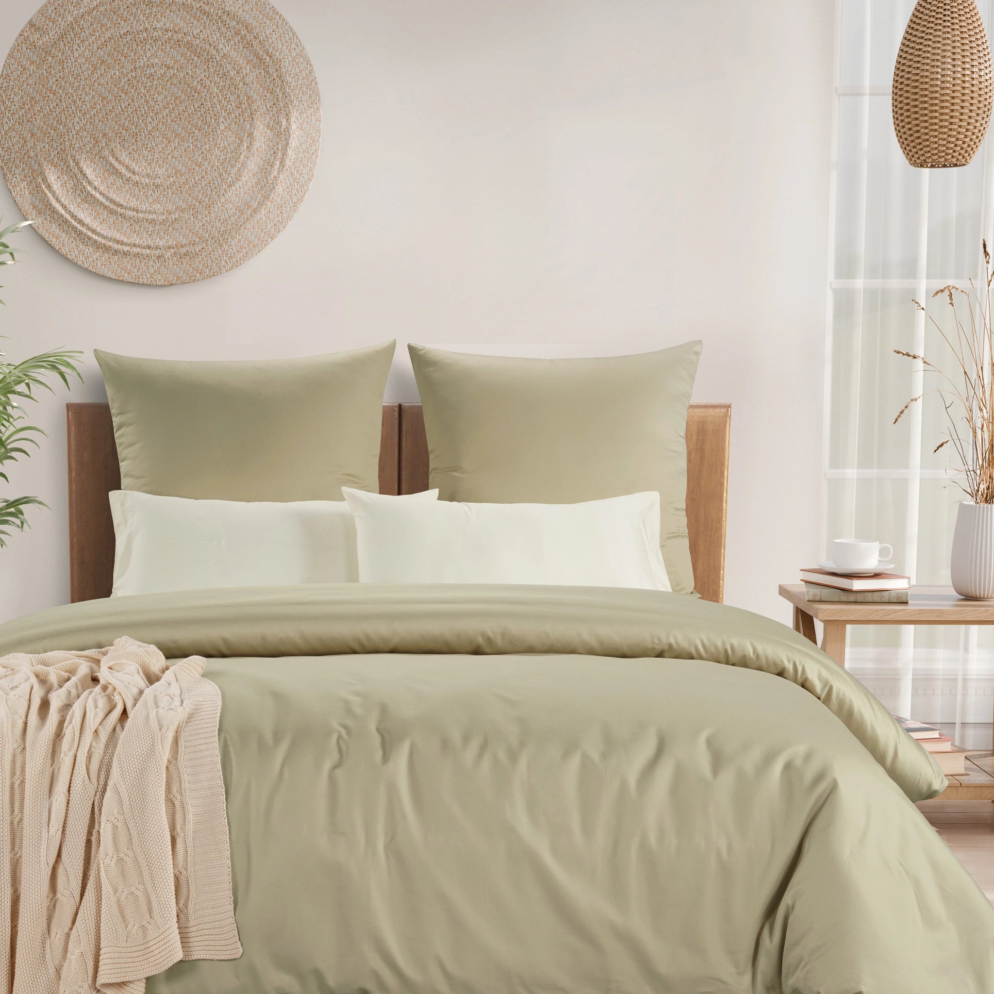 A neatly made bed with sage green bedding, including a duvet cover, two matching pillow shams, and two white accent pillows, styled in a bright, modern bedroom setting.