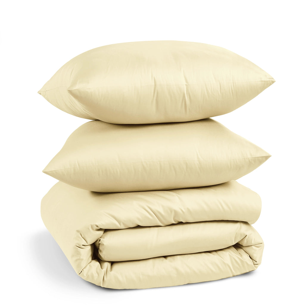A stack of three light beige pillows and a matching folded quilt or comforter on a clean white background.