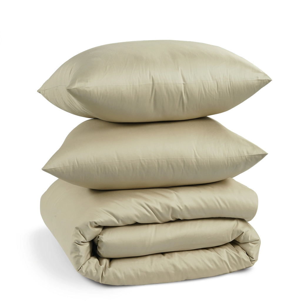 A stack of three light beige bedding items, including two pillows and a folded duvet or comforter, photographed on a clean white background.